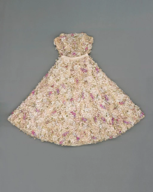 Strapless dress with floral embellishments in white, cream, and pink hues, photographed on a neutral grey background.