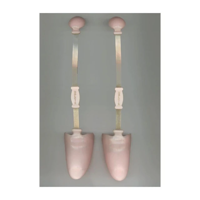 Pair of pink shoe stretchers on a grey background, showing the knob handles, tension rods, and shoe-shaped forms.