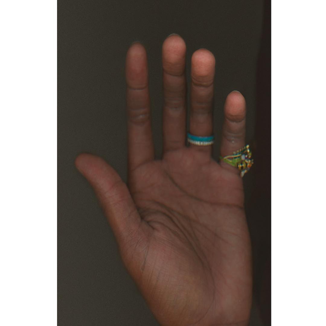 Close-up of an arm and hand with rings, capturing the texture of the skin and details of the colourful jewelry on fingers.