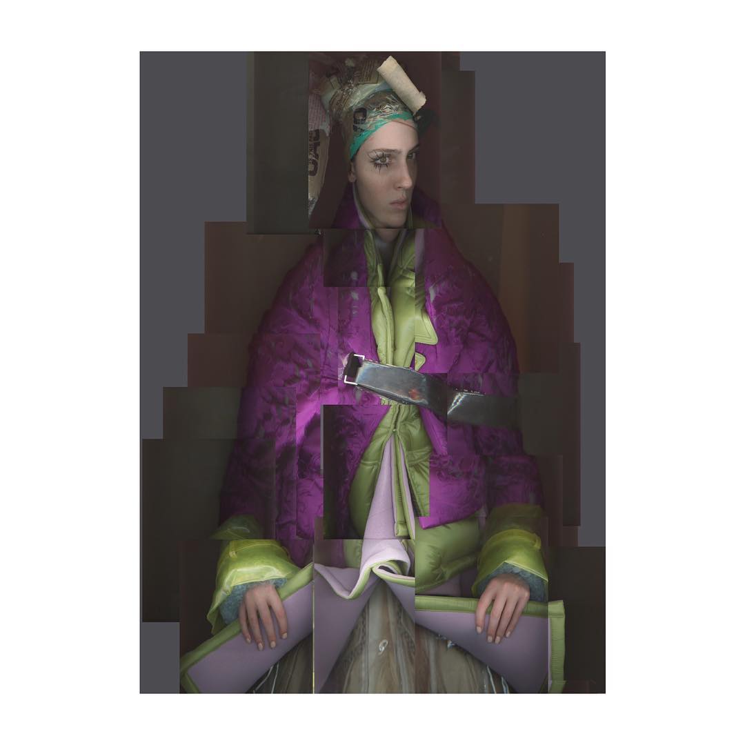 Woman in purple and green coat sits against mottled gray backdrop, head wrapped in patterned fabric, with dark eye makeup and neutral face.