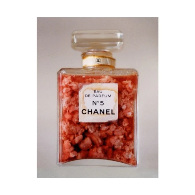 Square-shaped Chanel No. 5 perfume bottle filled with coral colored stones against a plain background in a studio shot.