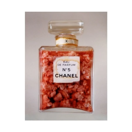 Square-shaped Chanel No. 5 perfume bottle filled with coral colored stones against a plain background in a studio shot.