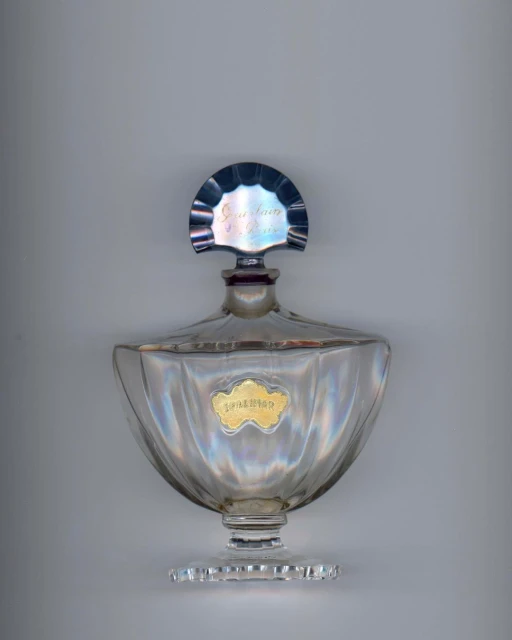 Elegant clear glass perfume bottle with a silver top and a gold label on a neutral background, showcasing vintage design.
