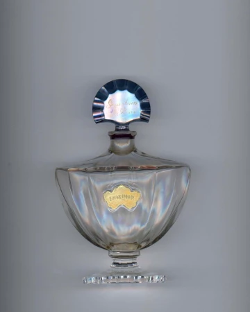 Elegant clear glass perfume bottle with a silver top and a gold label on a neutral background, showcasing vintage design.