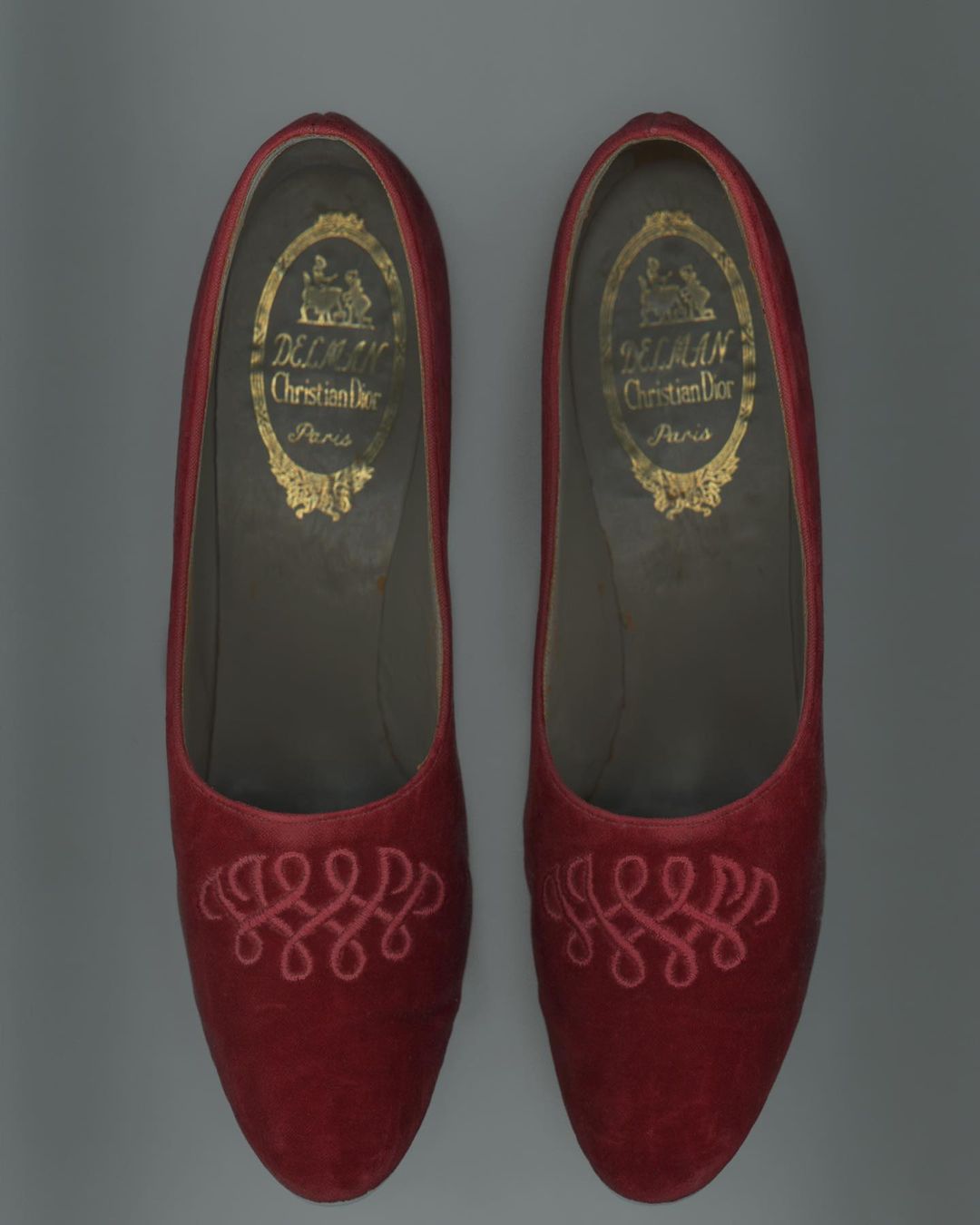 Pair of red Christian Dior slippers with intricate embroidery, showcasing vintage fashion footwear with designer brand logo on inner sole.