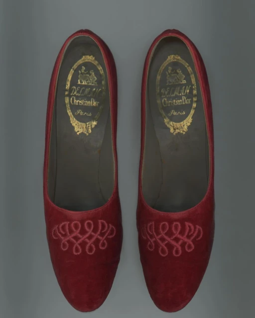 Pair of red Christian Dior slippers with intricate embroidery, showcasing vintage fashion footwear with designer brand logo on inner sole.