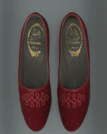 Pair of red Christian Dior slippers with intricate embroidery, showcasing vintage fashion footwear with designer brand logo on inner sole.
