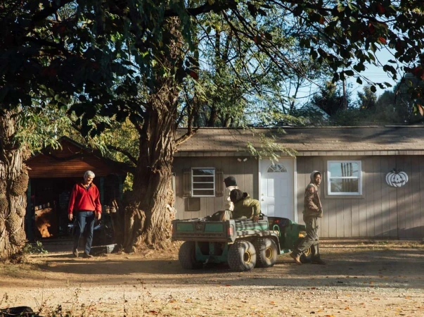 Three people in a yard with a utility vehicle in front of a building, with trees and blue sky visible during the daytime.