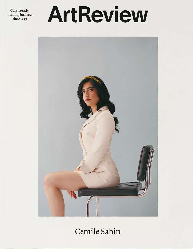 Magazine cover featuring a woman in a light-colored suit sitting on a black stool against a pale blue background, promoting art review.