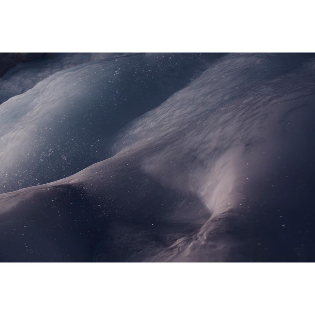 Icy landscape featuring snow-covered terrain with textured details and cool, blue-toned coloration, suggesting a glacial or arctic environment.