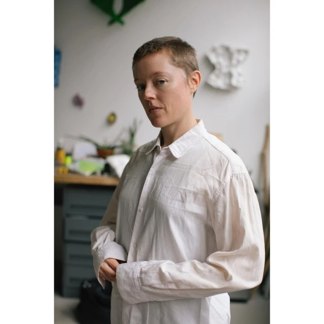 Portrait of an adult female with short hair wearing a button-down shirt, standing indoors against a neutral studio background.