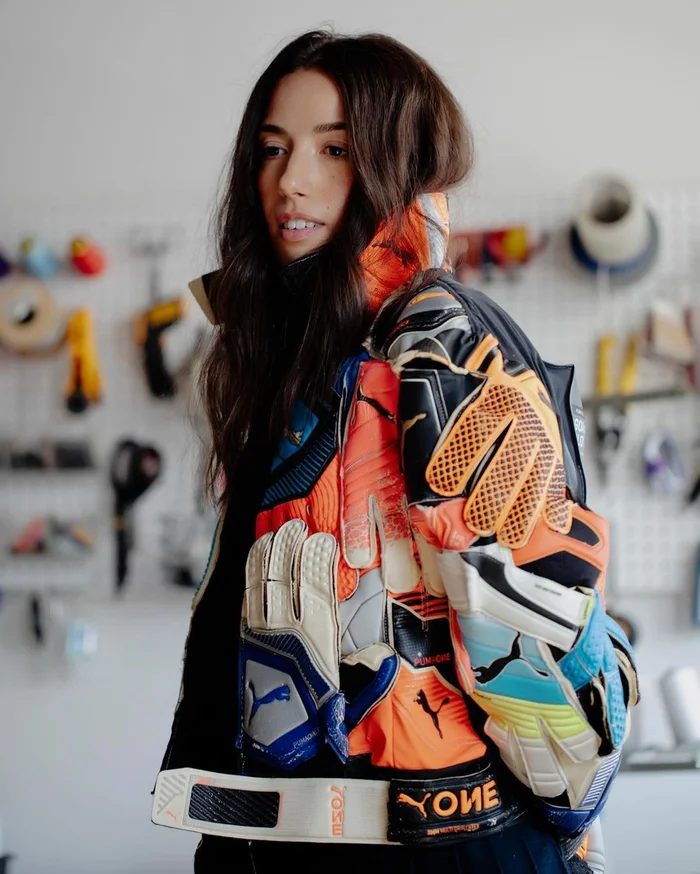 Woman wearing a colorful jacket made of stitched goalkeeper gloves and athletic materials in a studio setting.