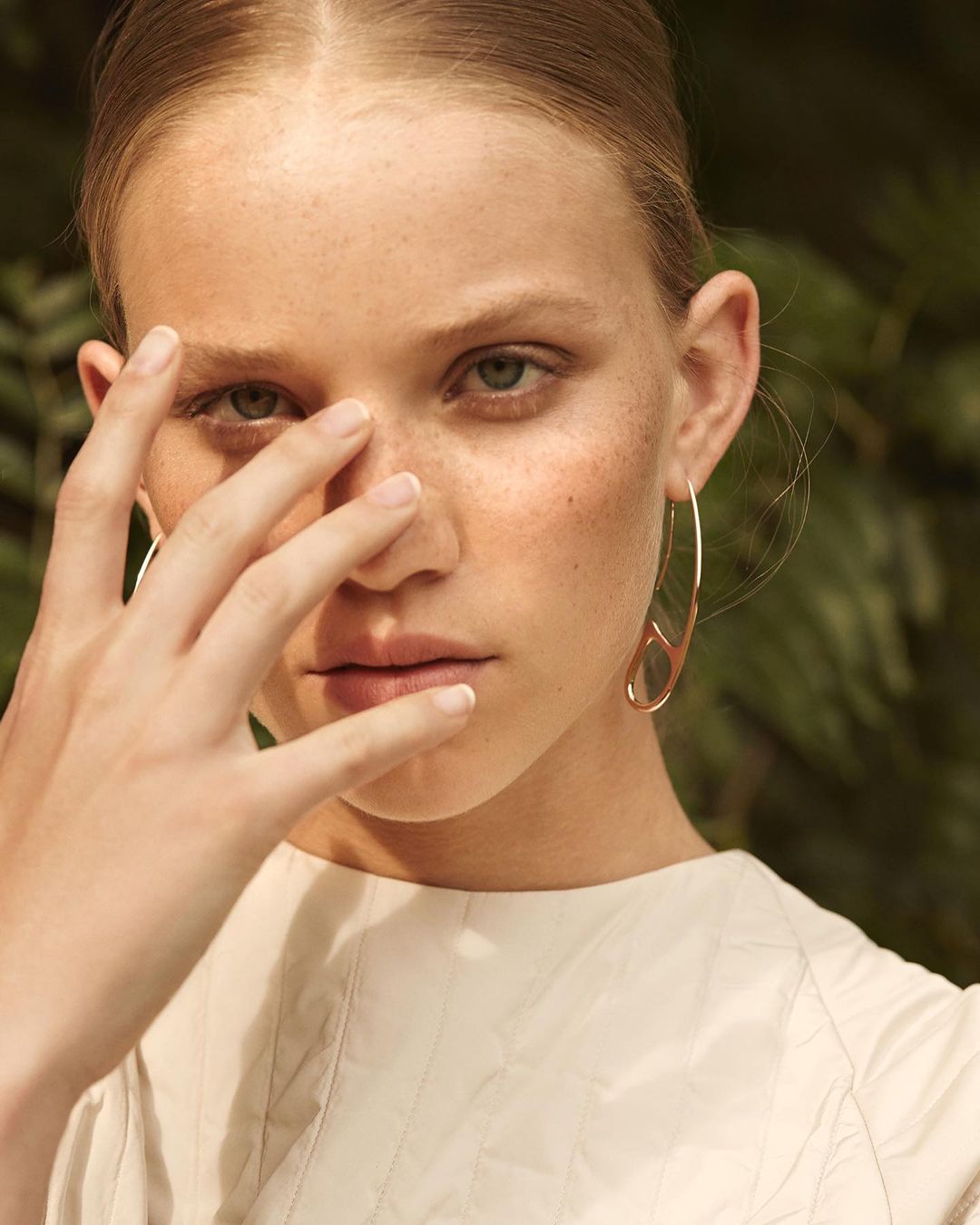 Close-up portrait of a woman with freckles holding her hand near her face wearing a gold earring