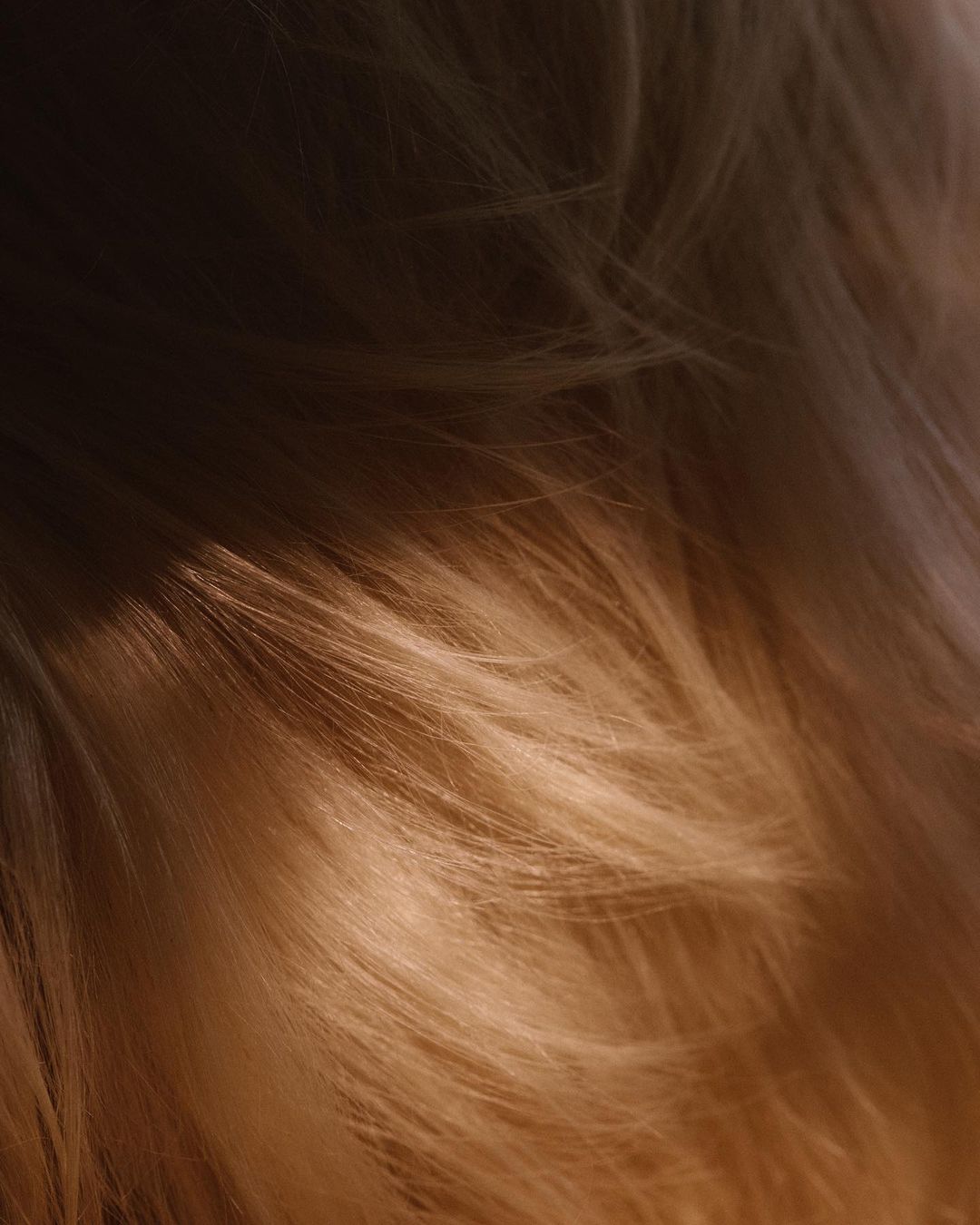 Close-up of flowing, silky long hair in warm, soft tones with light and shadow patterns creating depth and texture, fashion, and beauty.