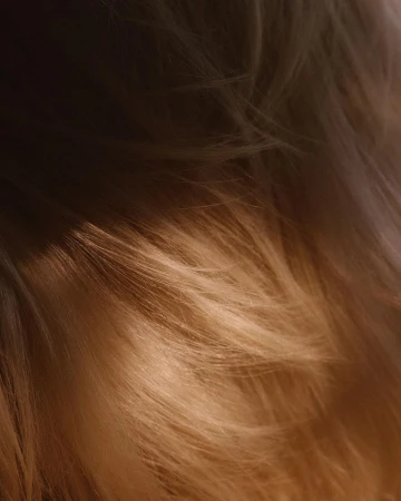 Close-up of flowing, silky long hair in warm, soft tones with light and shadow patterns creating depth and texture, fashion, and beauty.