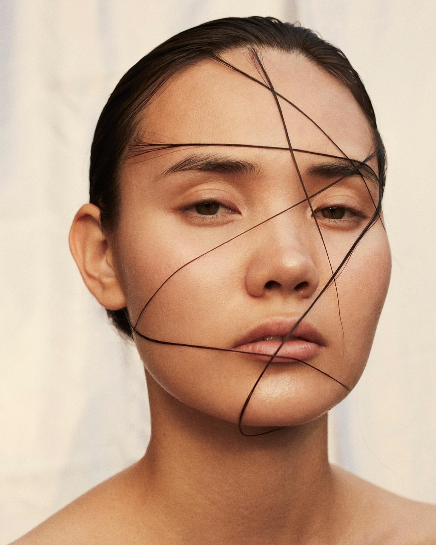 Close-up studio portrait of a woman with dark hair strands arranged across her face, highlighting her features and the smooth skin texture.