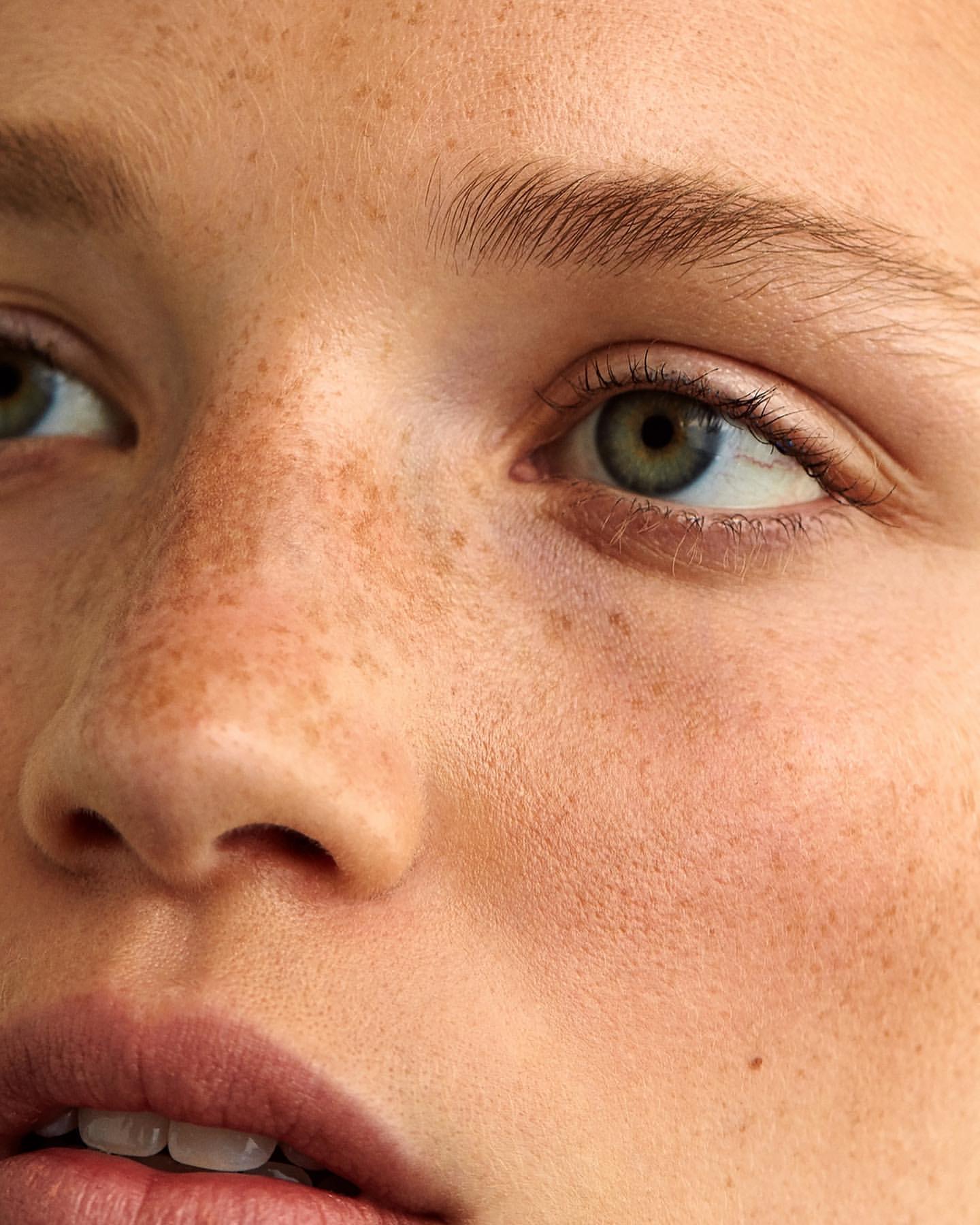 Close-up portrait of a young woman with fair skin and freckles. Her green eyes are visible and she's looking off to the side.