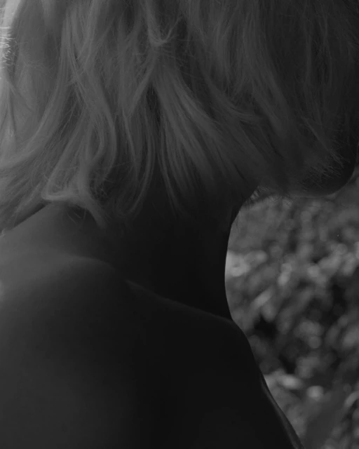 Monochrome portrait of an adult female with short blonde hair, revealing neck and upper back in an outdoor, natural light setting.