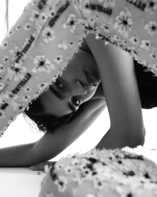 Close-up shot of an adult with floral-patterned clothing upside down, in a high-key lit, monochromatic indoor fashion setting.