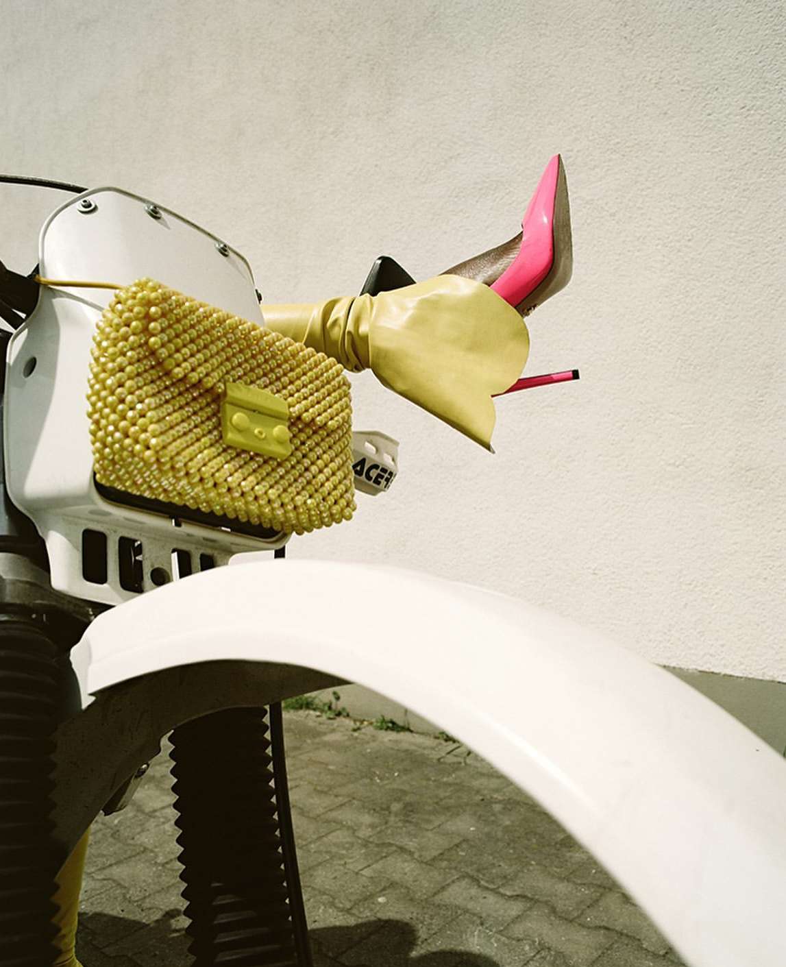 Fashion-forward motorcycle with a yellow beaded purse and pink stiletto heels. Yellow gloves add a playful touch to the vehicle's handlebars.