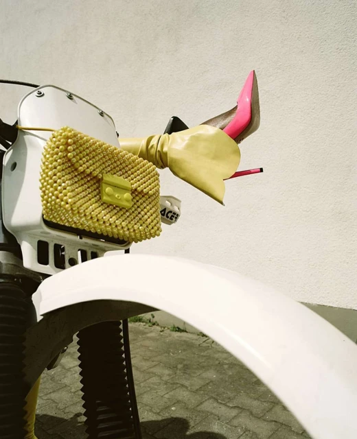 Fashion-forward motorcycle with a yellow beaded purse and pink stiletto heels. Yellow gloves add a playful touch to the vehicle's handlebars.