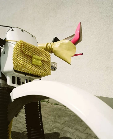 Fashion-forward motorcycle with a yellow beaded purse and pink stiletto heels. Yellow gloves add a playful touch to the vehicle's handlebars.