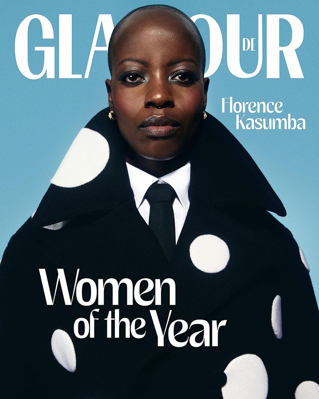Glamour magazine cover featuring Florence Kasumba in a black and white polka-dot jacket, tie, and a blue background. Text reads 'Women of the Year'.