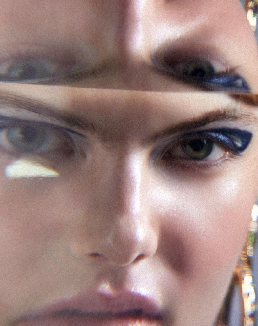 Close-up portrait of a woman's face with striking blue eyeliner, viewed through a distorting prism, creating a surreal effect on her features.