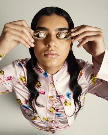 Close-up portrait of a woman wearing pearled decorative hair clips over her eyes and a pink patterned blouse