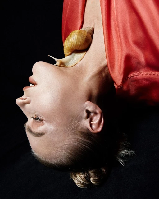 Dramatic beauty shot of a woman with a snail on her neck against a dark background, showcasing unique editorial fashion and skincare.