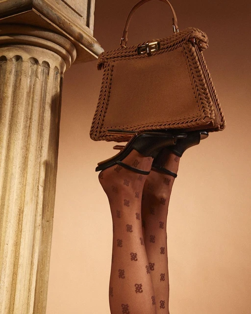 Upside down view of legs in patterned tights, black heels, and a brown handbag against a neutral backdrop and ionic column.