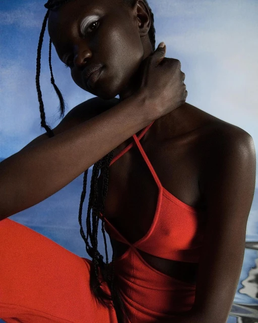 Portrait of an African-American woman in a red jumpsuit with a halter top. The woman has dark braided hair and white eyeshadow.