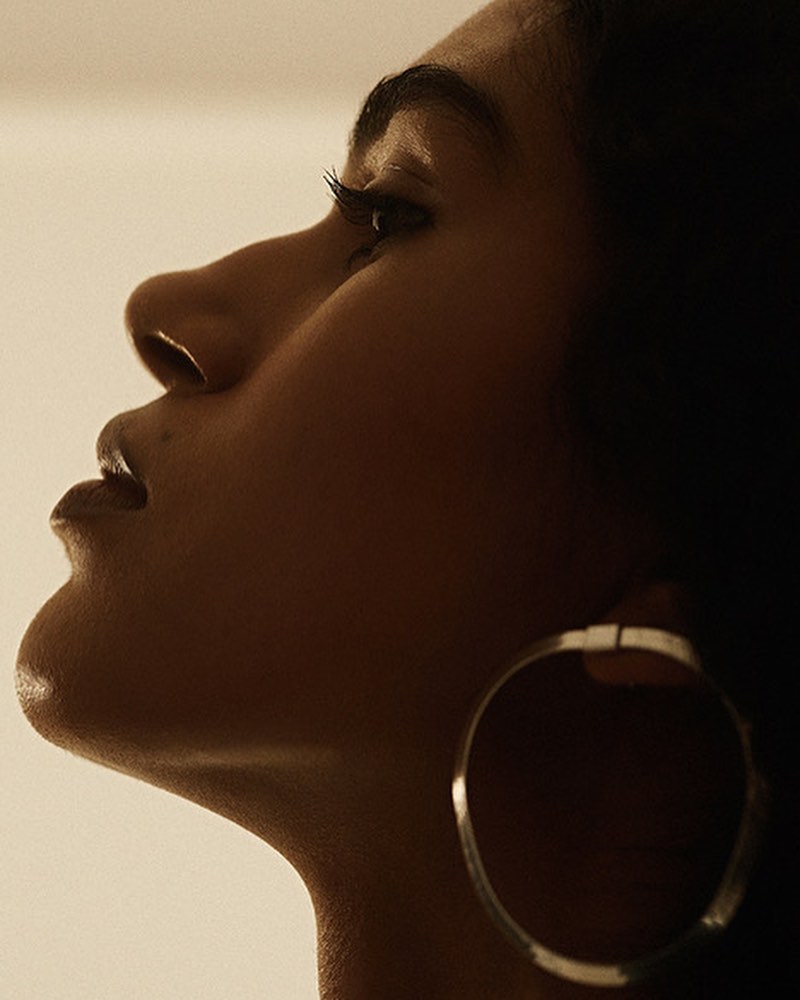 Profile portrait of a Black woman with hoop earring looking upward in studio lighting showcasing skin tone, facial features, and earring.
