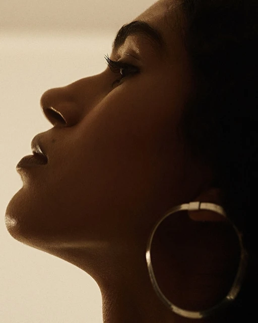Profile portrait of a Black woman with hoop earring looking upward in studio lighting showcasing skin tone, facial features, and earring.
