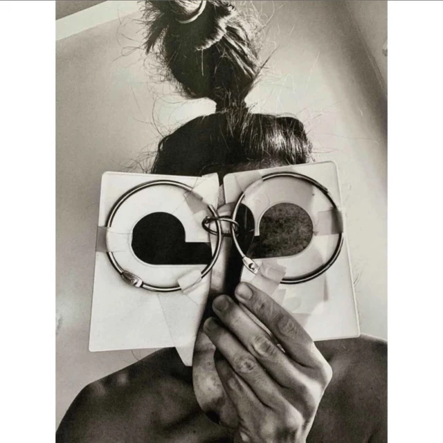 Black and white portrait of a person holding white cards with circular cutouts in front of their face, obscuring their features.