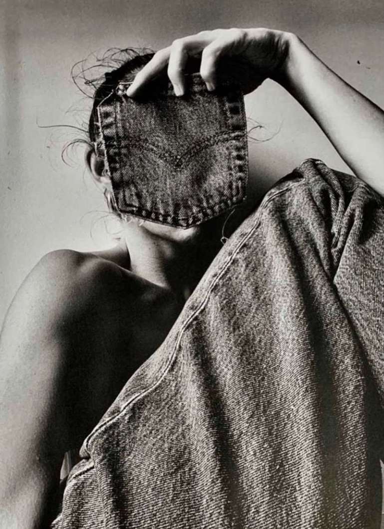 Monochrome portrait of a person obscured by a denim pocket, seated with jeans draped, creating an artistic fashion statement.