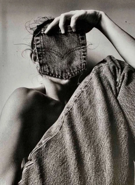 Monochrome portrait of a person obscured by a denim pocket, seated with jeans draped, creating an artistic fashion statement.