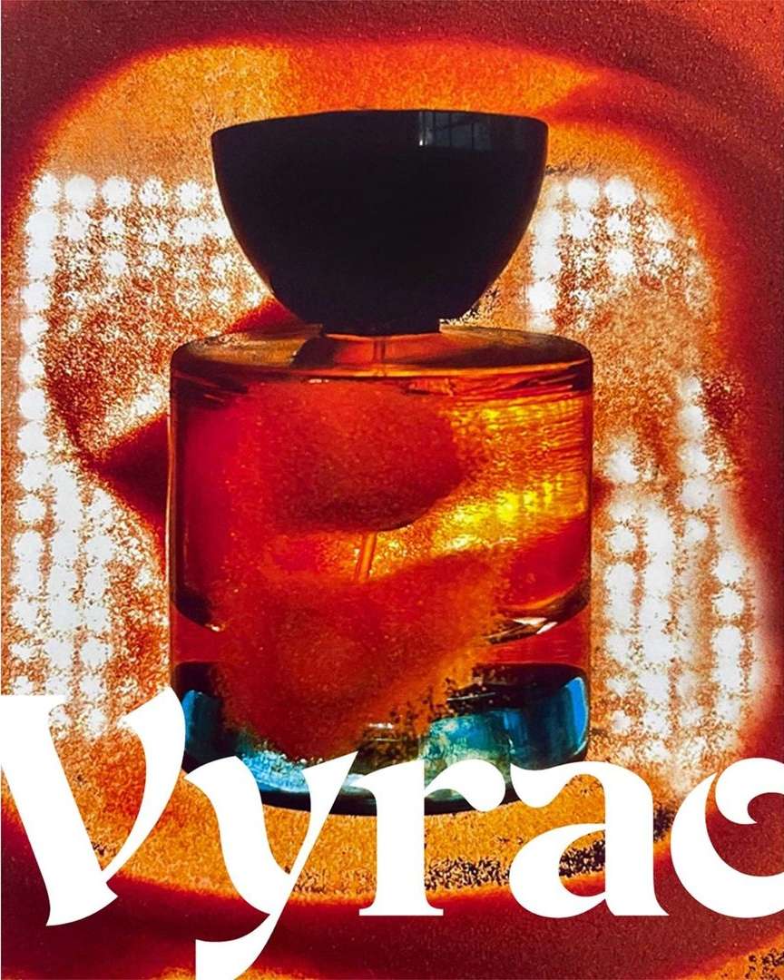 Close-up product shot of a translucent amber perfume bottle with a dark cap against an abstract fiery red background