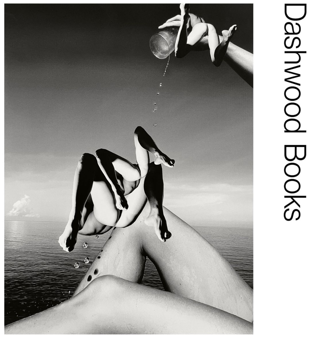 Black and white photographic collage of human limbs and torso against the sky and ocean, with a glass of water being poured.