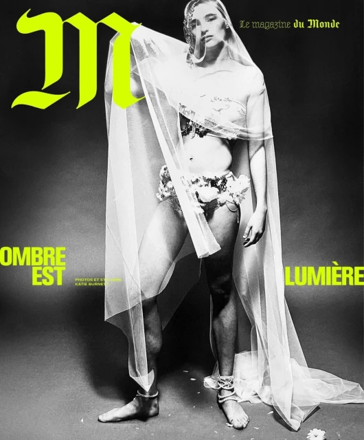 Magazine cover featuring a woman in floral decor and sheer fabric, against a dark background with bright lettering and high-contrast lighting.