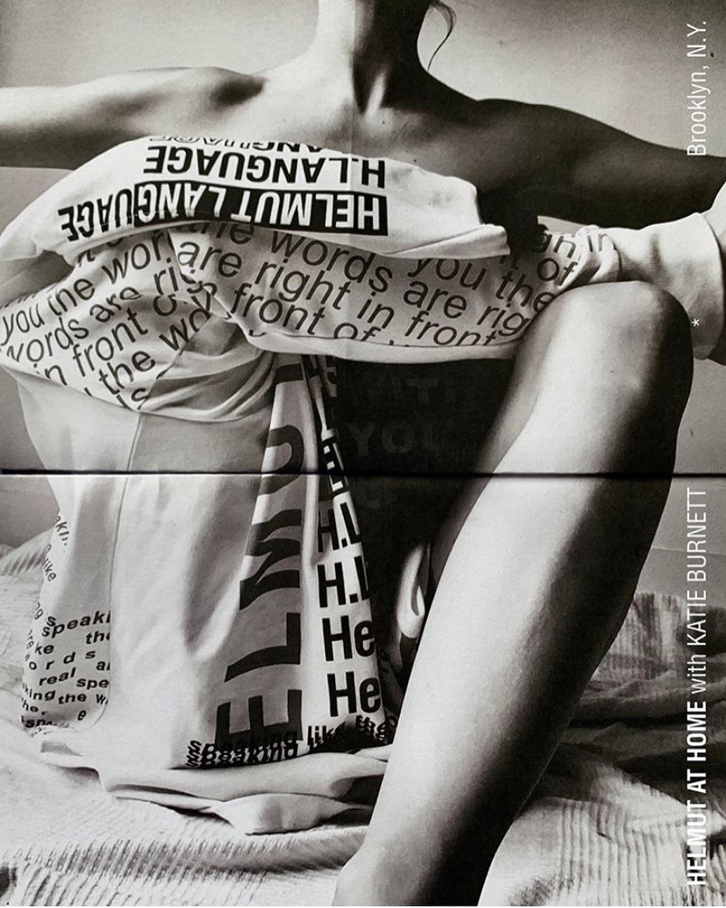 Monochrome portrait of a seated person wrapped in printed white fabric featuring bold typography