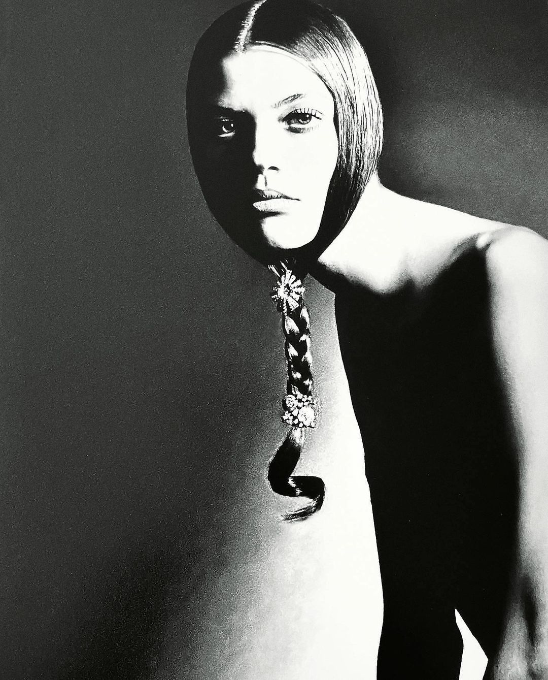 Monochromatic portrait of a young adult female model with a braided hairstyle decorated with jewels against a gray background in studio lighting.