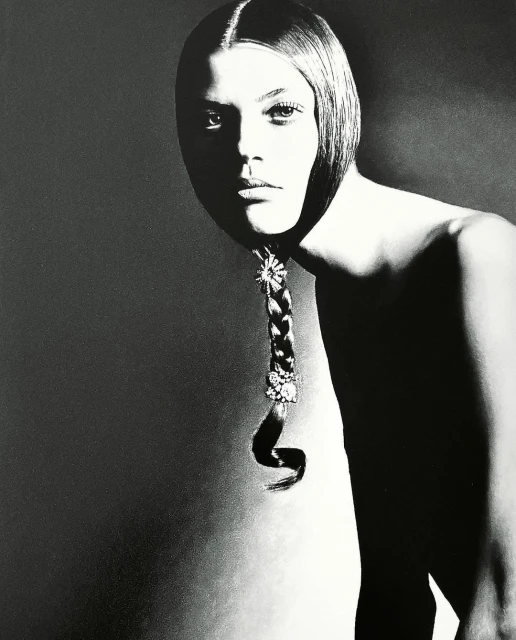 Monochromatic portrait of a young adult female model with a braided hairstyle decorated with jewels against a gray background in studio lighting.