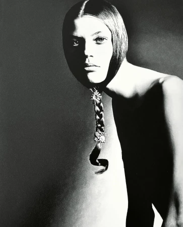 Monochromatic portrait of a young adult female model with a braided hairstyle decorated with jewels against a gray background in studio lighting.