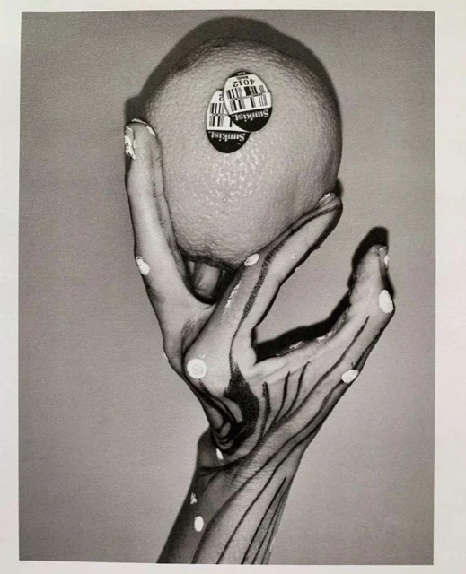 Monochrome art photograph of a hand with painted linear details holding a Sunkist orange, captured in a studio setting with soft lighting.