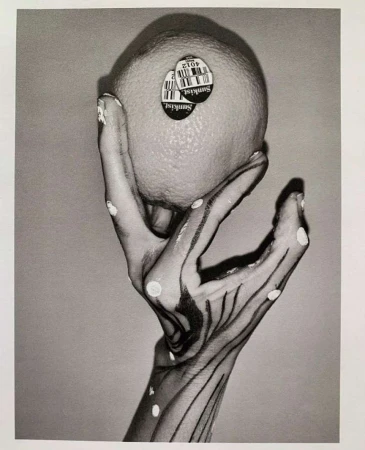 Monochrome art photograph of a hand with painted linear details holding a Sunkist orange, captured in a studio setting with soft lighting.