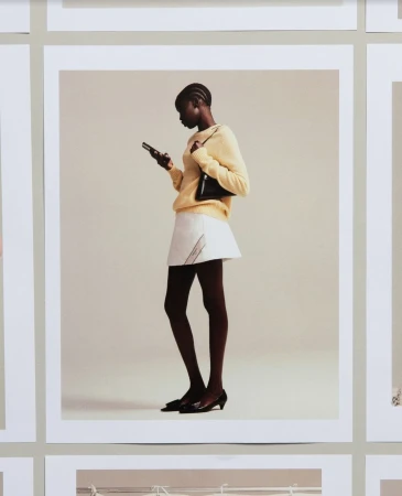 Black woman in a yellow sweater and white skirt holding a smartphone against a pale background
