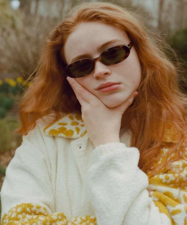 Portrait of young woman with red hair wearing sunglasses and a patterned cream and yellow coat outdoors