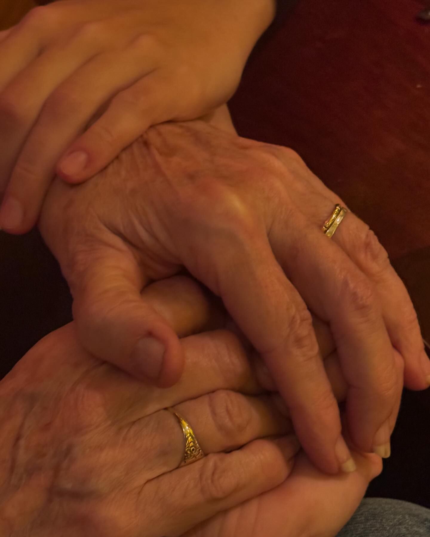Close-up of older adult and young adult hands intertwined, featuring gold rings, suggesting connection, family, and generational love.