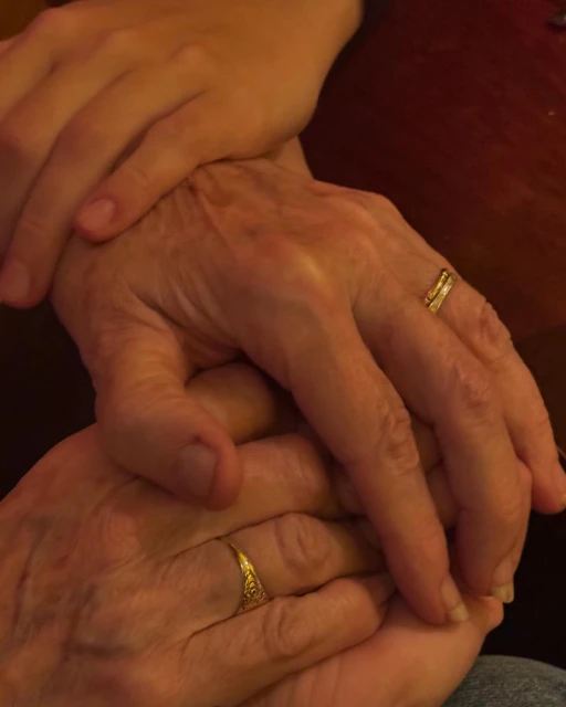 Close-up of older adult and young adult hands intertwined, featuring gold rings, suggesting connection, family, and generational love.